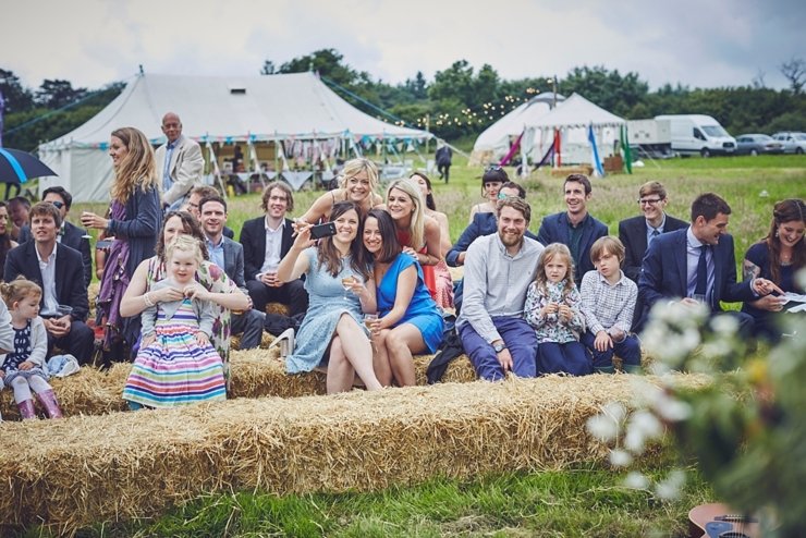 guests on hay bales at outdoor wedding blessing in Dorset