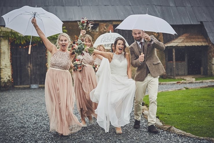 wedding party running laughing with umbrellas at a rainy wedding in Devon