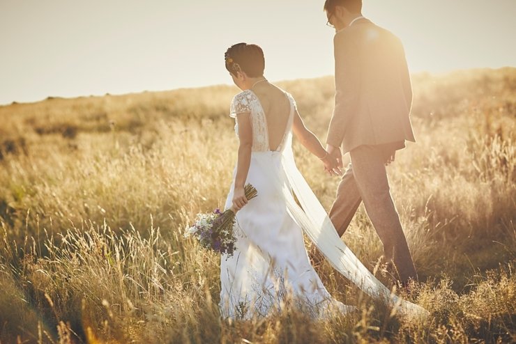bride and groom walk through wheat field in the golden hour sunset