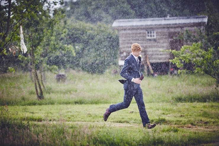 Groom running in the rain at a boho outdoor wedding in Dorset