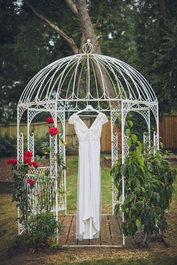 wedding gown hanging from rose covered pergola 